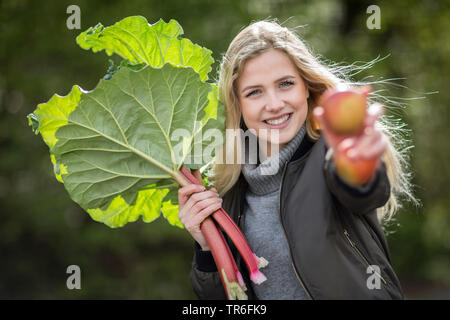 rhubarb (Rheum rhabarbarum), young blond woman with fresh picked rhubarb and apples, Germany