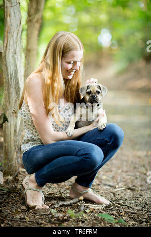 domestic dog (Canis lupus f. familiaris), crouching young woman holding a cute Puggle on the lap, Germany Stock Photo