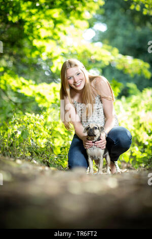 domestic dog (Canis lupus f. familiaris), good looking young woman with a Puggle, kneeing on forest ground, Germany Stock Photo