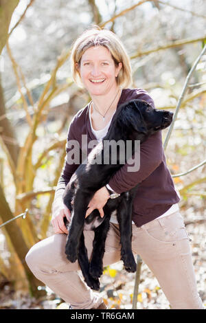 Flat Coated Retriever (Canis lupus f. familiaris), woman with whelp in a forest, Germany Stock Photo