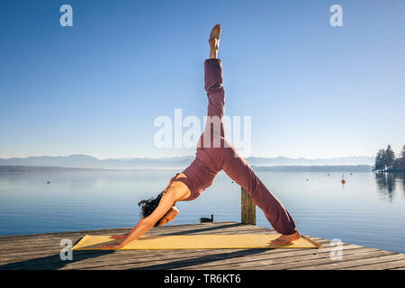 woman doing yoga exercises at a lake. leg high, downward facing dog, Germany, Bavaria Stock Photo