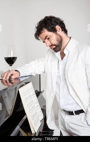 young man in white suit standing at a piano, Germany Stock Photo