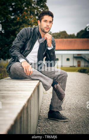 young attractive man with leather jacket sitting on a park bench, Germany Stock Photo
