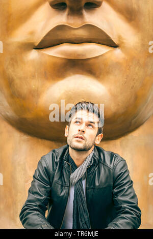 young attractive man with leather jacket sitting under a mouth of a large sculpture, Germany Stock Photo