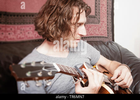 young man playing guitar on sofa, Germany Stock Photo