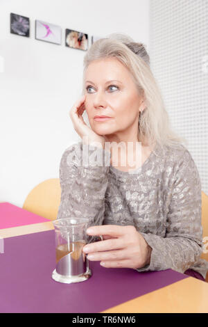 female senior sitting at the desk and drinking tea, Germany Stock Photo