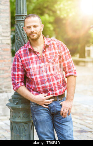 handsome man with checkered skirt in a city, leaning at a lantern, Germany Stock Photo