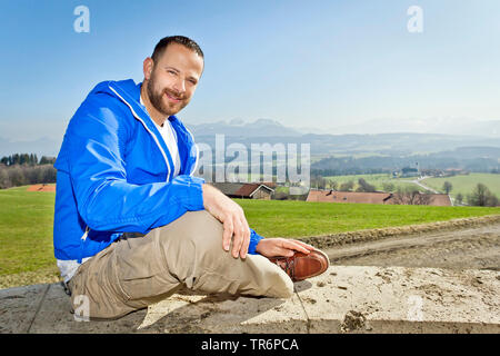 handsome man sitting on a wall in the mountains, Germany, Bavaria Stock Photo