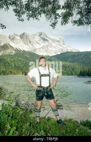 nice good looking man in Bavarian traditional clothing standing at the lakeside of the Eibsee, Zugspitze in the background, Germany, Bavaria Stock Photo