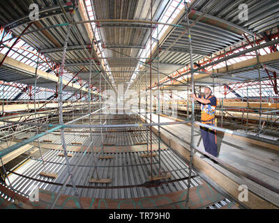 A scaffolder makes adjustments to an access structure within the roof of Earls Court station in London, UK, during revovation works. Fish-eye lens. Stock Photo