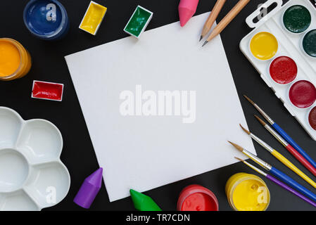 Concept of creativity: composition with small blank white canvas, surrounded by brushes, paints and palette on a black background, with space for text Stock Photo