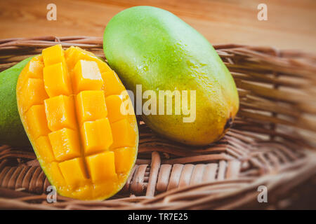 Close-up of fresh green Dashehari mangoes and its slice placed in wooden basket on wooden table.