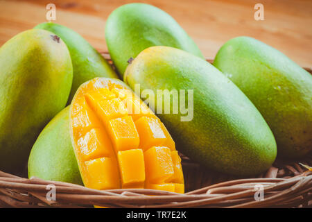 Close-up of fresh green Dashehari mangoes and its slice placed in wooden basket on wooden table.