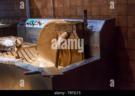 Machine processes and creation of chocolate in dark room. Pouring milk chocolate Stock Photo