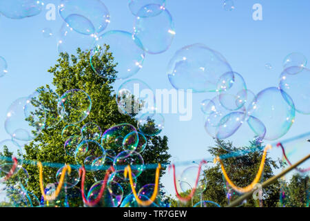 Blurred big soap bubbles flying in air by blue sky, sunny day in city. Blurry abstract summer background. Concept of funny party. Defocused fantasy so Stock Photo