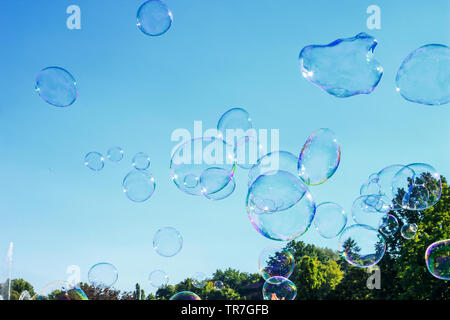 Lot of big soap bubbles flying in air by blue sky, sunny day in city. Abstract summer background. Concept happy childhood or funny party. Fantasy soap Stock Photo