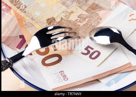 Banknotes 50 and 10 euros are in a white plate with a blue border. On top of them are a fork and spoon. The concept of wealth and success Stock Photo