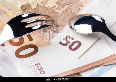 Banknotes 50 and 10 euros are in a white plate. On top of them are a fork and spoon. The concept of the cost of healthy eating Stock Photo