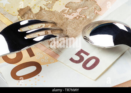 Banknotes 50 and 10 euros are in a white plate with a blue border. On top of them are a fork and spoon. The concept of taxation on individual business Stock Photo