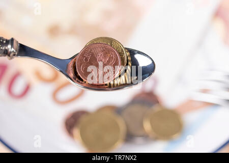 Euro coins in a dessert spoon over a plate of money with a blue border. The concept of Bank interest rates and betting Stock Photo
