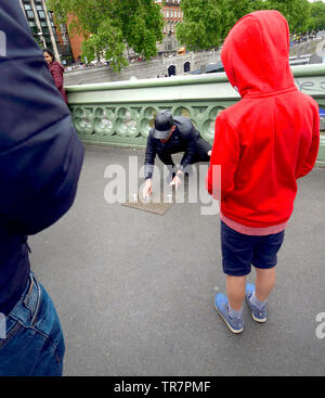 London, England, UK. Illegal Cup and Ball / 3 Cups Trick on Westminster Bridge, trying to con money from passing tourists - child watching