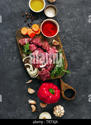 Sliced beef fillet with vegetable. kitchen table with сuts meat and veggies on dark table top view. Ingredients cooking meat Stock Photo