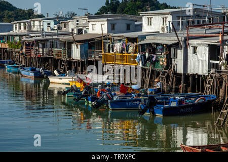 A Fisherman Mends Nets Outside Colourful Houses On Stilts, Tai O Fishing Village, Hong Kong, China Stock Photo