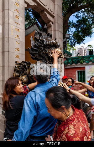 Chinese Tourists Rub The Dragon Statue For Good Luck At The Entrance To Wong Tai Sin Temple, Hong Kong, China Stock Photo