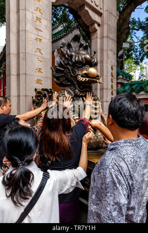 Chinese Tourists Rub The Dragon Statue For Good Luck At The Entrance To Wong Tai Sin Temple, Hong Kong, China Stock Photo