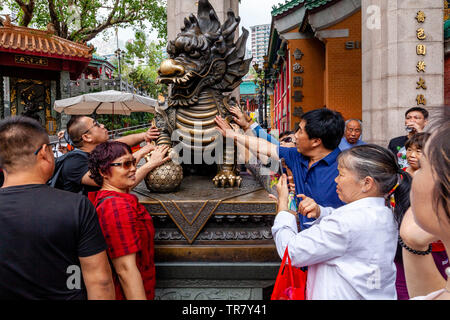 Chinese Tourists Rub The Dragon Statue For Good Luck At The Entrance To Wong Tai Sin Temple, Hong Kong, China Stock Photo