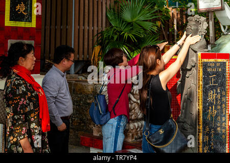 Chinese Tourists Rub The God Of Wealth Statue To Bring Good Fortune, Kwun Yam Shrine, Repulse Bay, Hong Kong, China Stock Photo