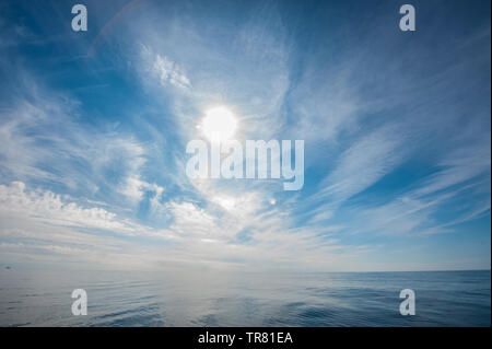 Noon sun shining through cirrus clouds over the open calm ocean. Stock Photo