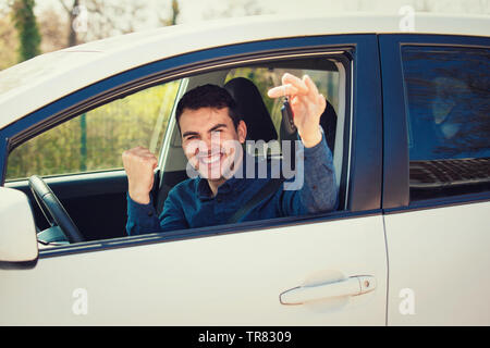 Casual guy driver showing car keys out of the window. Successful young man bought a new car, holding fist up tight celebrating triumph. Rental cars or Stock Photo