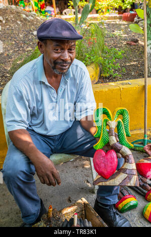 Local shopkeeper holding a wooden carvings that he made to sell to tourists at a local craft market, Ocho Rios, Jamaica, Caribbean Stock Photo