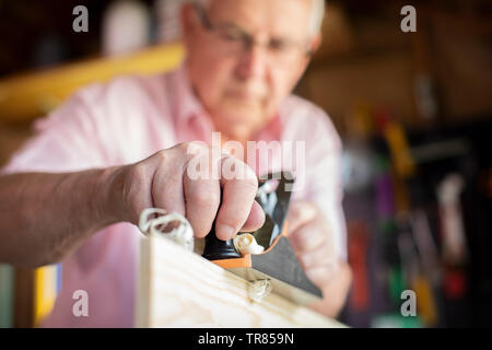 Senior Man Enjoying Carpentry Planing Wood In Garden Shed Stock Photo