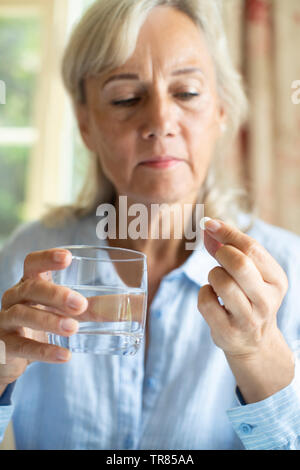 Senior Woman Taking Tablet With Glass Of Water At Home Stock Photo