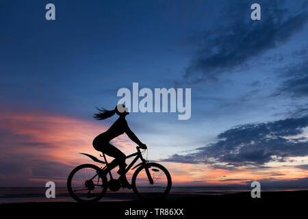Silhouette photo of young woman riding on bicycle with sunset cloudy sky in background