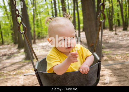 adorable blond caucasian toddler in the swing at the playground Sorel-Tracy pointing finger Stock Photo