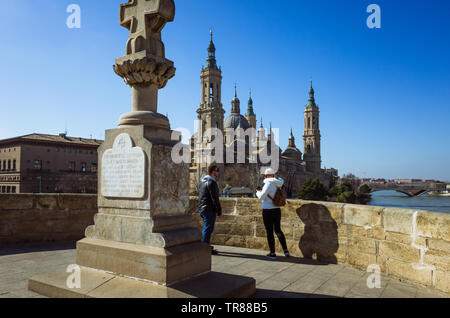 Zaragoza, Aragon, Spain : Two people stand on the Puente de Piedra (Stone Bridge) across the river Ebro with the Basilica of Our Lady of the Pillar in Stock Photo