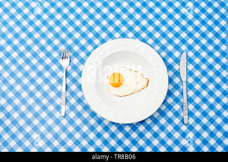 White plate with single fried egg on blue and white pattern tablecloth Stock Photo