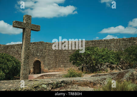 Big cross made of stone over rocky terrain and large wall with gateway at Sortelha. An astonishing and well preserved medieval hamlet in Portugal. Stock Photo