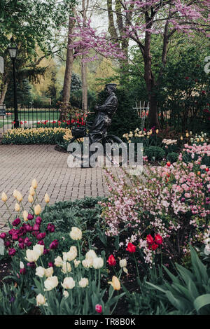 Pella, Iowa, USA - May 2, 2019: Sculpture of a Dutch man with his bicycle in Scholte Gardens. Variety of spring flowers and multicolored tulips. Stock Photo