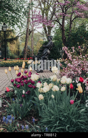 Pella, Iowa, USA - May 2, 2019: Sculpture of a Dutch man with his bicycle in Scholte Gardens. Variety of spring flowers and multicolored tulips. Stock Photo