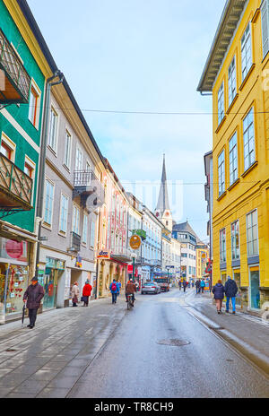 BAD ISCHL, AUSTRIA - FEBRUARY 20, 2019: Historic Pfarrgasse shopping street with dense colorful edifices and tall belfry of the Parish Church on backg Stock Photo