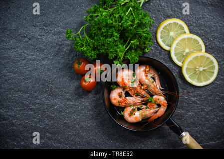 Seafood plate with shrimps prawns cooked on pan with herbs and spices lemon tomato and curly parsley on dark background Stock Photo