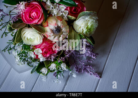 Closeup of a bouquet of various flowers of buttercups, gray, roses, tulips on a light wooden surface, selective focus, free space for text Stock Photo