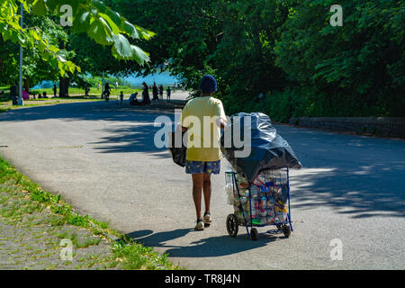Lady is pulling cart with used empty bottles and cans through the park for deposit. Stock Photo