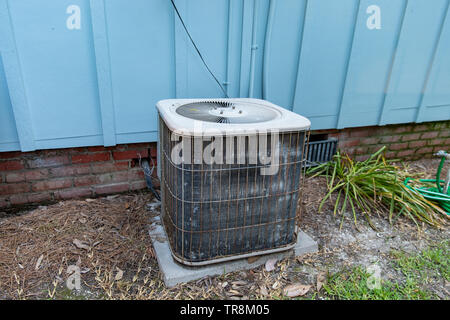 Old air conditioner system compressor next to home, needing maintenance. Stock Photo