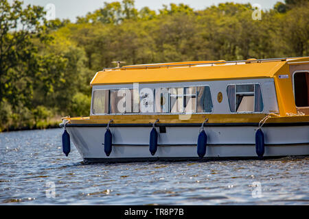 May 2019: Wroxham Broad, Norfolk – Tourists on a Richardsons hire boat motoring across Wroxham Broad between sailing boat races on a bright and sunny Stock Photo