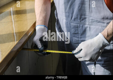 Worker is checking the correctness of the installation of a window sill. He is measuring the distance from the wall to the edge of the sill. Stock Photo